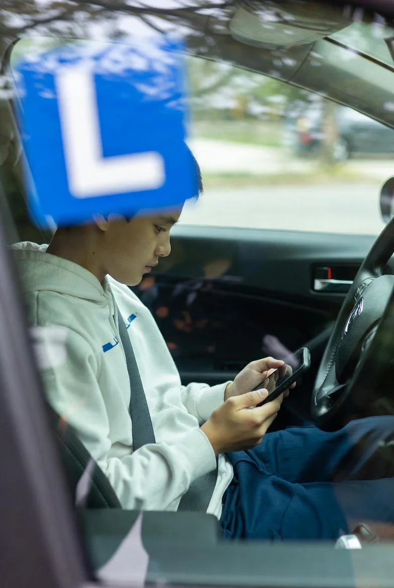 Conductor novel joven con el distintivo L en el coche, consultando su seguro de coche por primera vez